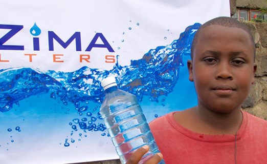 Boy holding a bottle of dirty water alongside uzima clean water