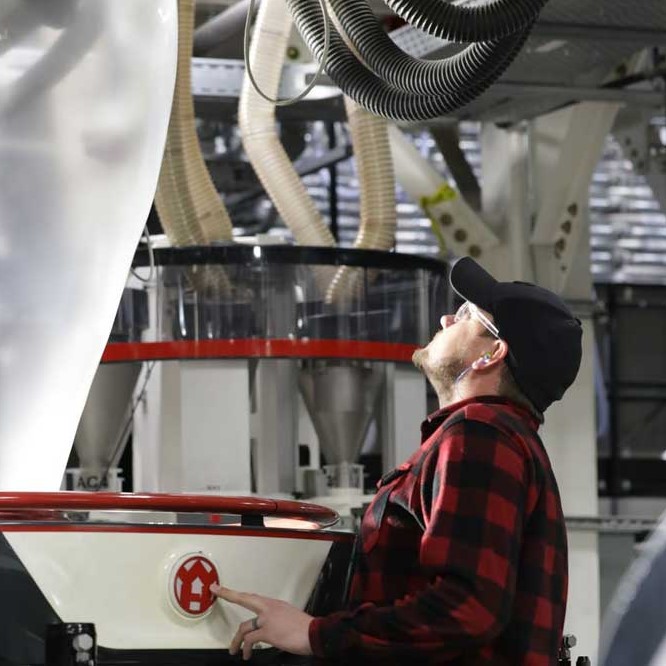 A person is operating a blown film extrusion machine inside a warehouse.